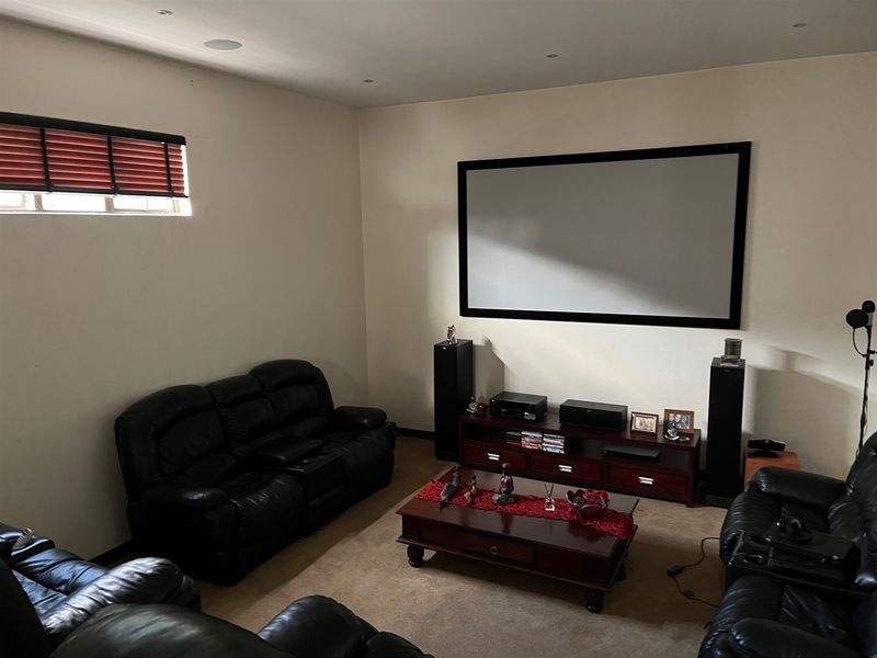 A dedicated cinema room featuring a wall-mounted projector screen, recessed ceiling lighting, and integrated audio speakers for an immersive home entertainment experience.