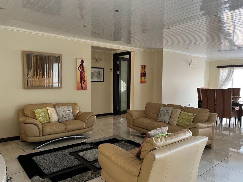 Spacious open-plan living and dining area featuring glossy ceiling finishes, recessed lighting, and neutral porcelain floor tiles throughout.
