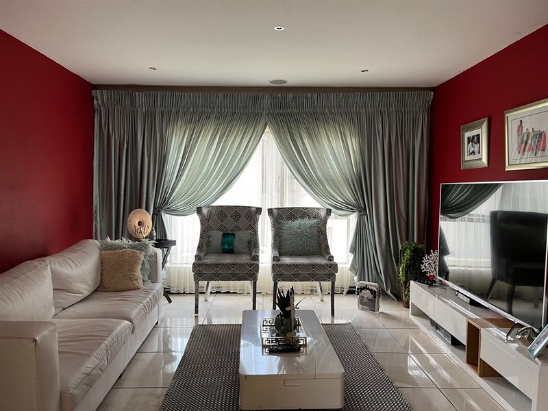 A well-maintained living room featuring polished porcelain floor tiles, recessed downlighting, and floor-to-ceiling curtain treatments.