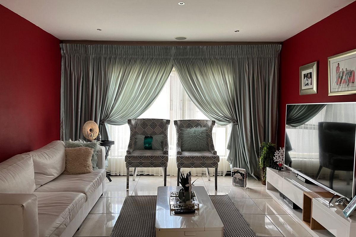 A well-maintained living room featuring polished porcelain floor tiles, recessed downlighting, and floor-to-ceiling curtain treatments.