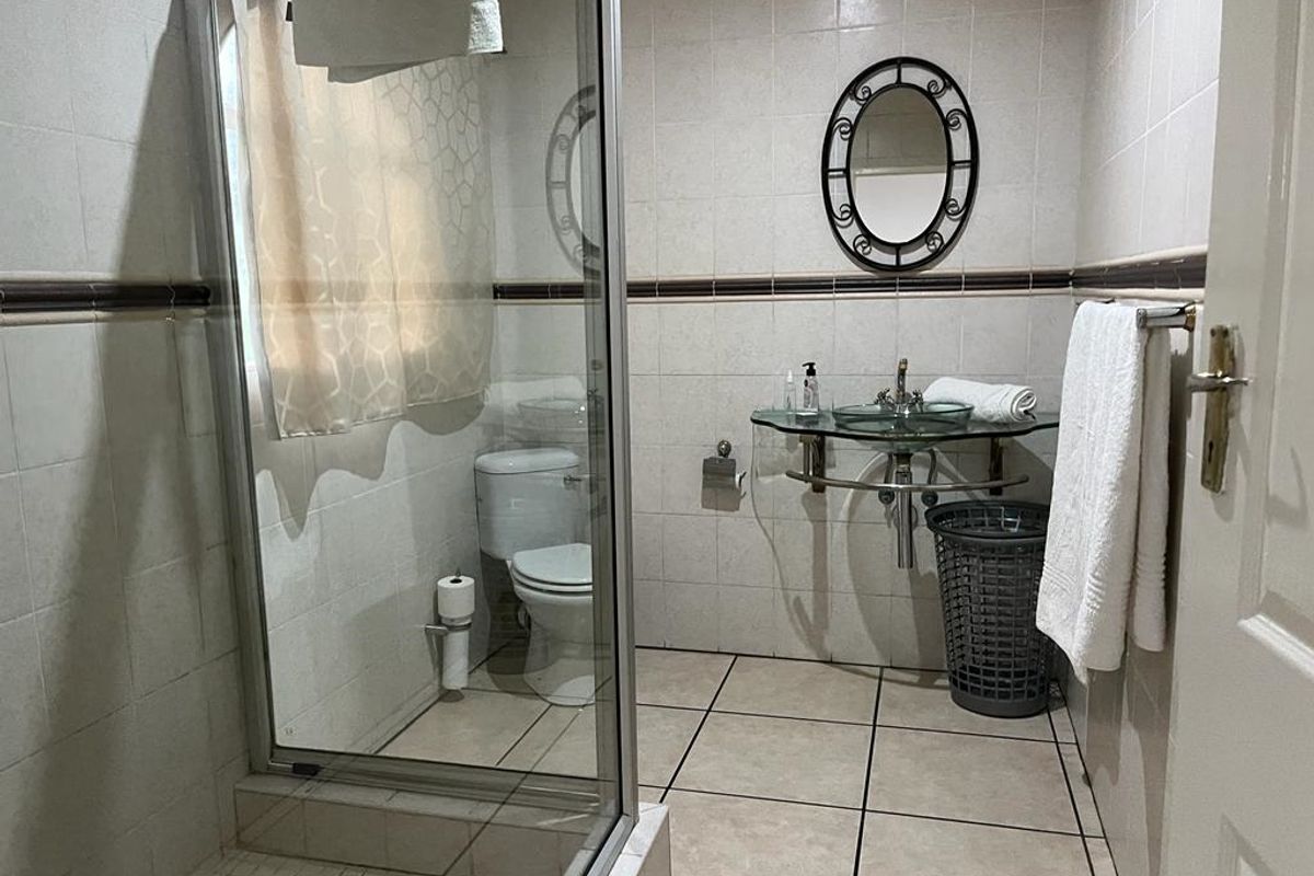 A functional bathroom featuring a glass shower enclosure, a wall-mounted glass vanity basin, and full-height wall tiling.