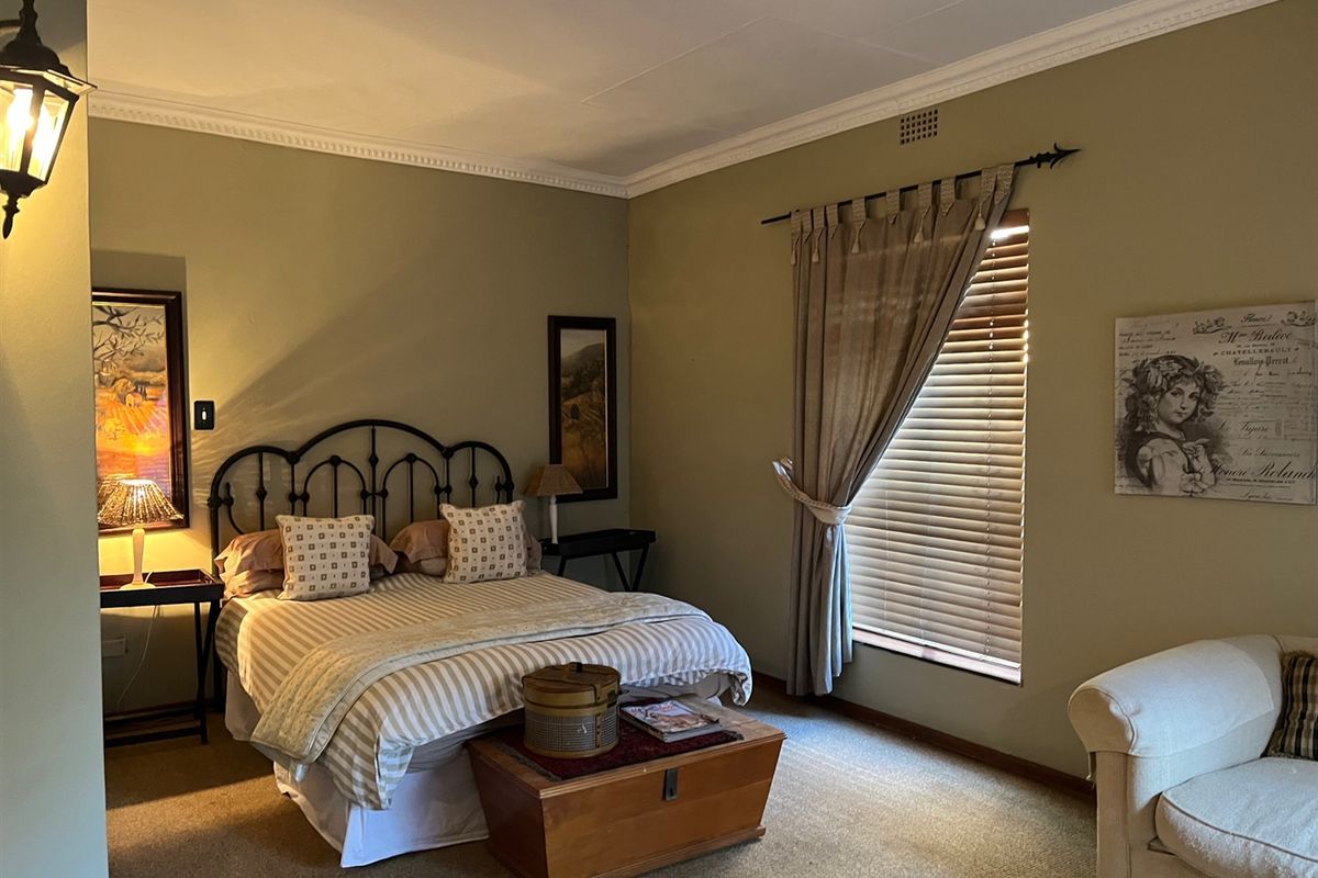 A cozy bedroom featuring neutral wall tones, crown molding, and a window fitted with wooden blinds, providing a comfortable and functional sleeping space.