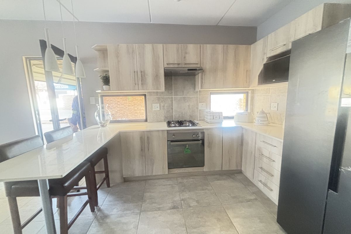 Modern kitchen featuring light wood-finish cabinetry, stone countertops, a breakfast bar, and integrated gas hob and oven, with tiled flooring throughout.