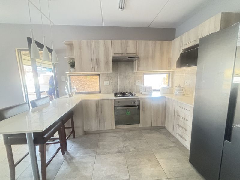Modern kitchen featuring light wood-finish cabinetry, stone countertops, a breakfast bar, and integrated gas hob and oven, with tiled flooring throughout.