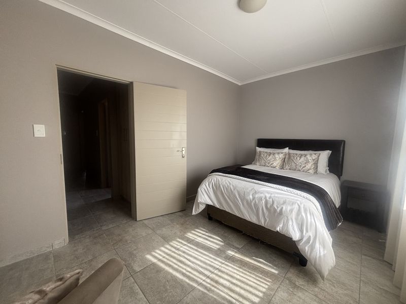 A well-maintained bedroom featuring neutral wall tones, tiled flooring, and a clean, modern horizontal panel door.
