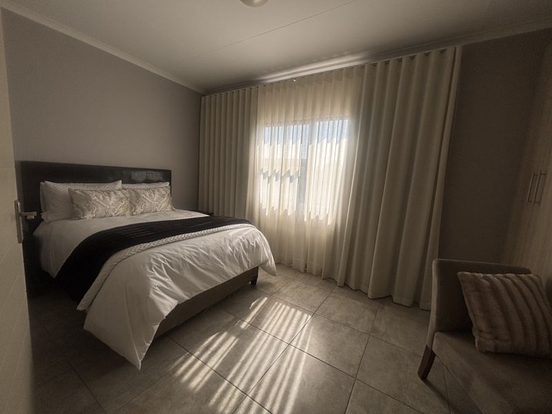 A well-maintained bedroom featuring tiled flooring, built-in cupboards, and floor-to-ceiling curtains that allow for soft natural light.