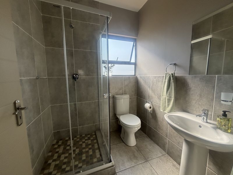 A clean and modern bathroom featuring a glass-enclosed shower, pedestal sink, and neutral floor-to-ceiling tiling.
