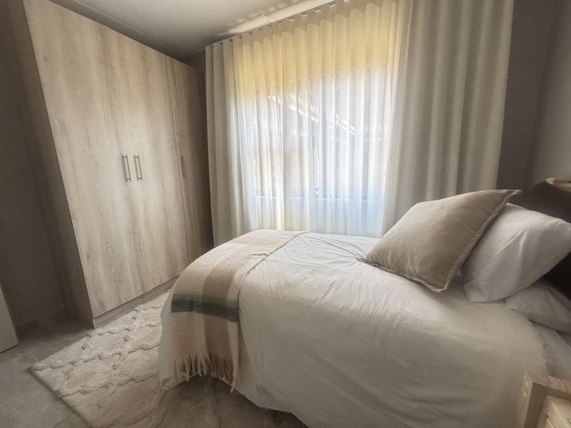 A well-maintained bedroom featuring a large built-in wardrobe with light wood-grain finish and floor-to-ceiling curtain tracks.