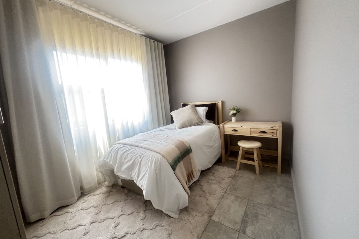 A well-lit bedroom featuring neutral wall tones, tiled flooring, and large windows with installed curtain tracks.