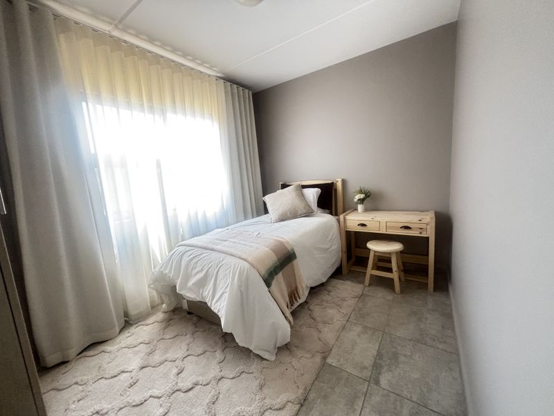 A well-lit bedroom featuring neutral wall tones, tiled flooring, and large windows with installed curtain tracks.