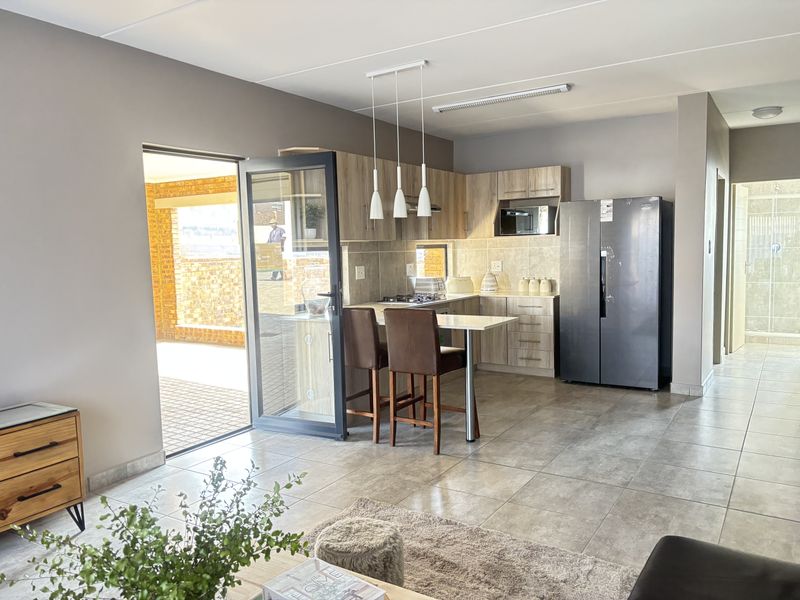 Modern open-plan kitchen featuring light wood cabinetry, integrated appliances, and a breakfast bar, seamlessly connecting to the outdoor patio area.
