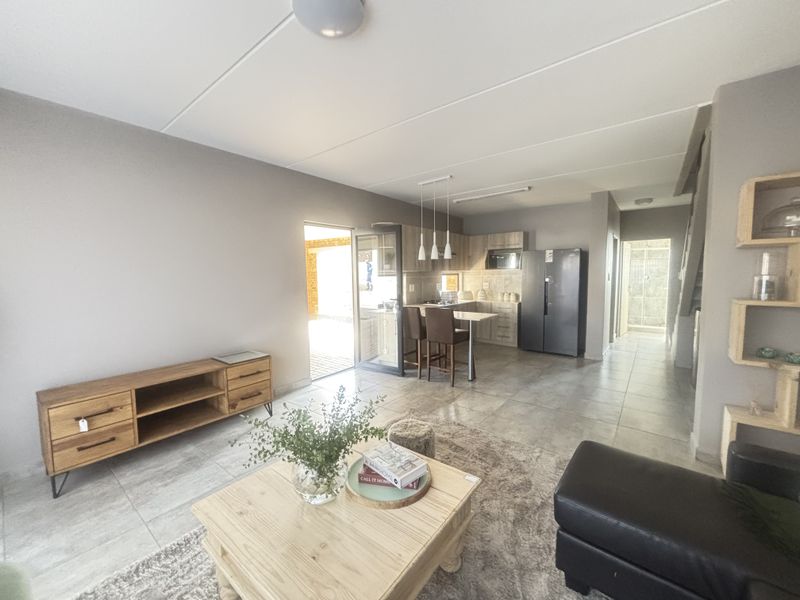 Spacious open-plan living area featuring tiled floors, a modern kitchen with built-in cabinetry, and a breakfast counter, leading to an outdoor patio.