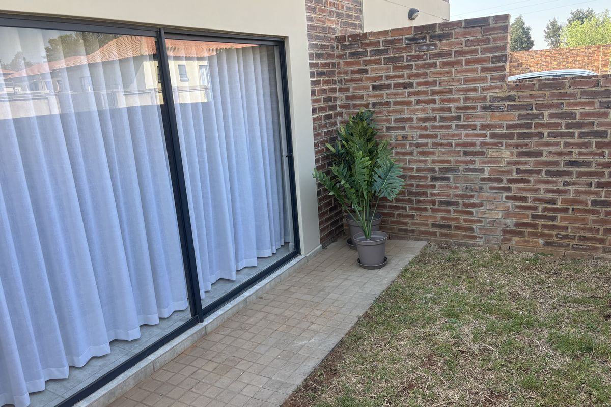 A private rear courtyard featuring a paved patio area, sliding glass door access, and a sturdy brick boundary wall.