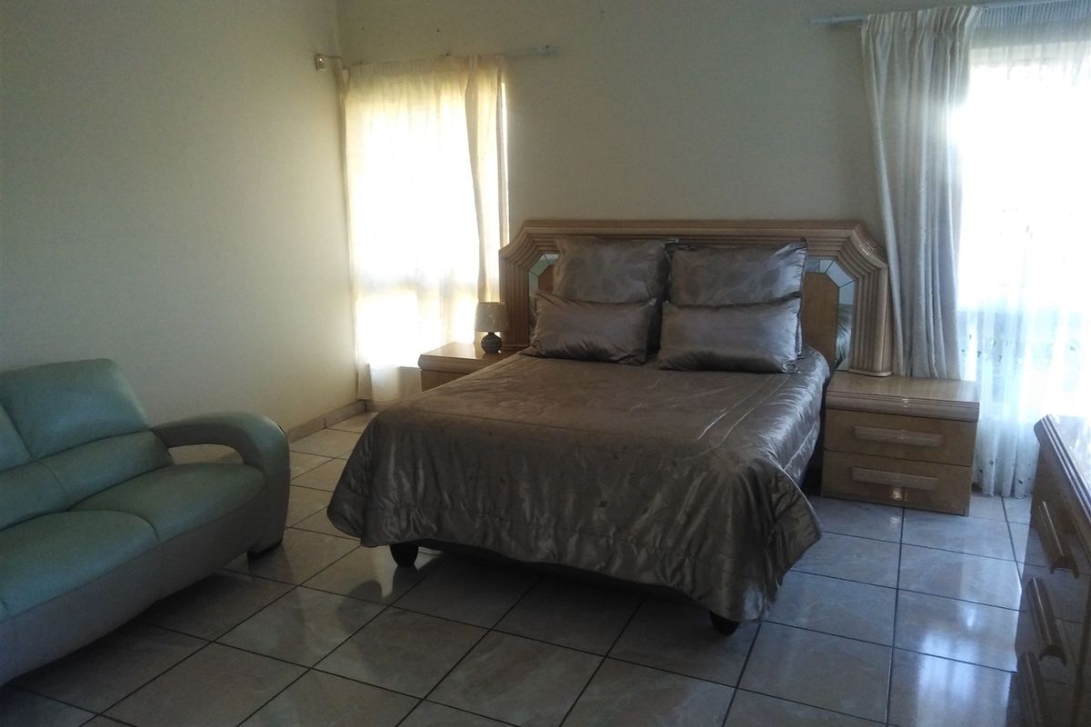 A spacious bedroom featuring tiled flooring and a built-in headboard with integrated bedside tables, offering a functional layout with natural light.