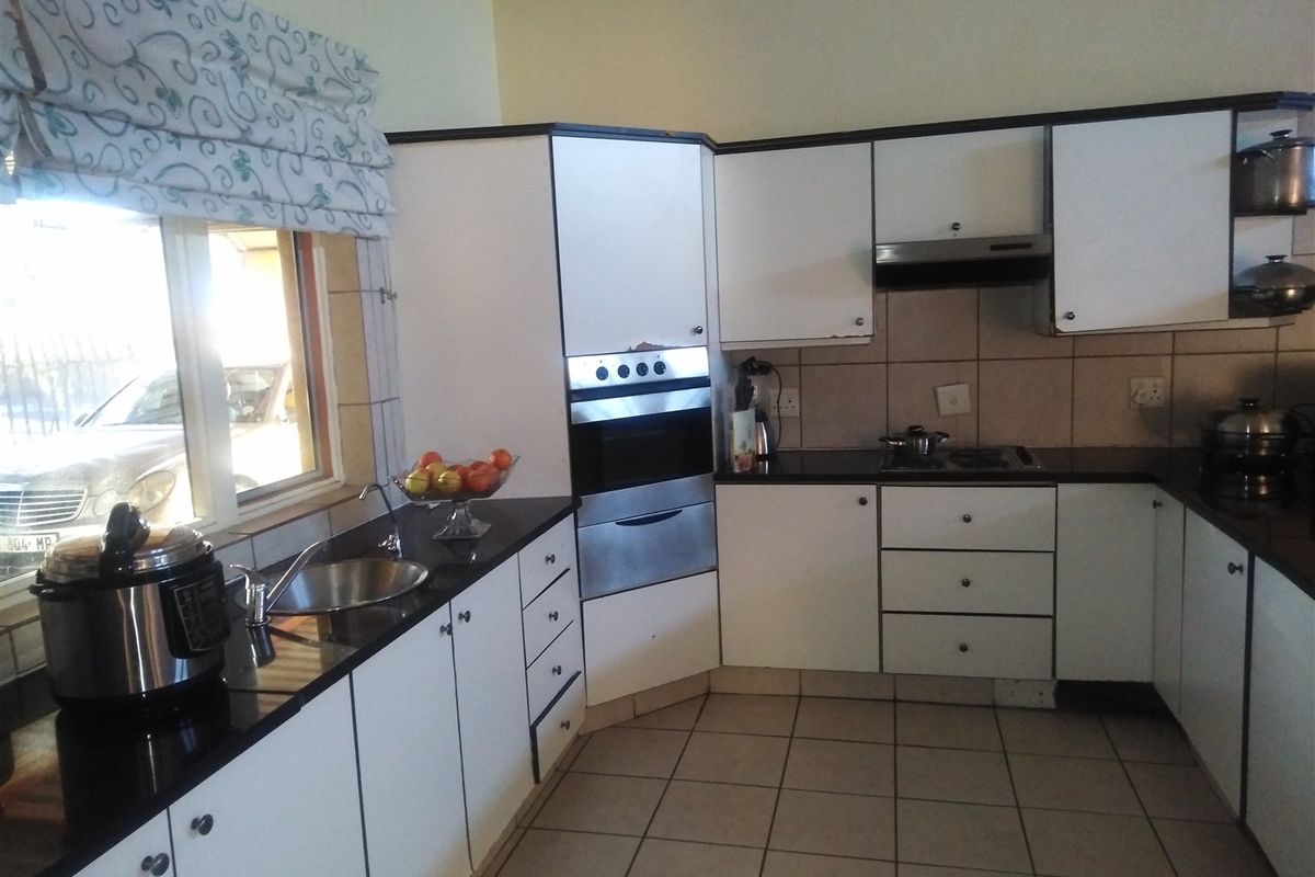 A functional kitchen featuring white cabinetry, dark stone countertops, tiled flooring, and built-in appliances including an oven and extractor fan.