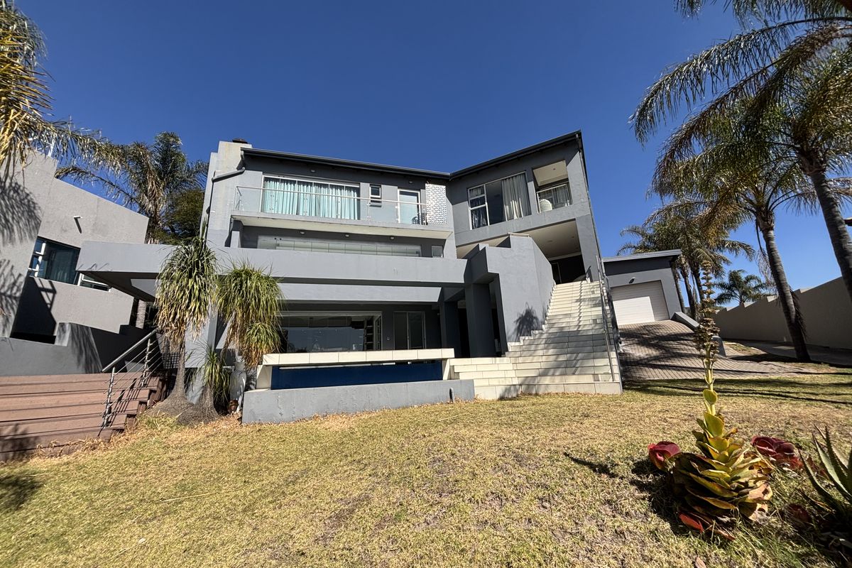Rear view of a multi-story modern house featuring a swimming pool, elevated balcony, external staircase, and attached garage.