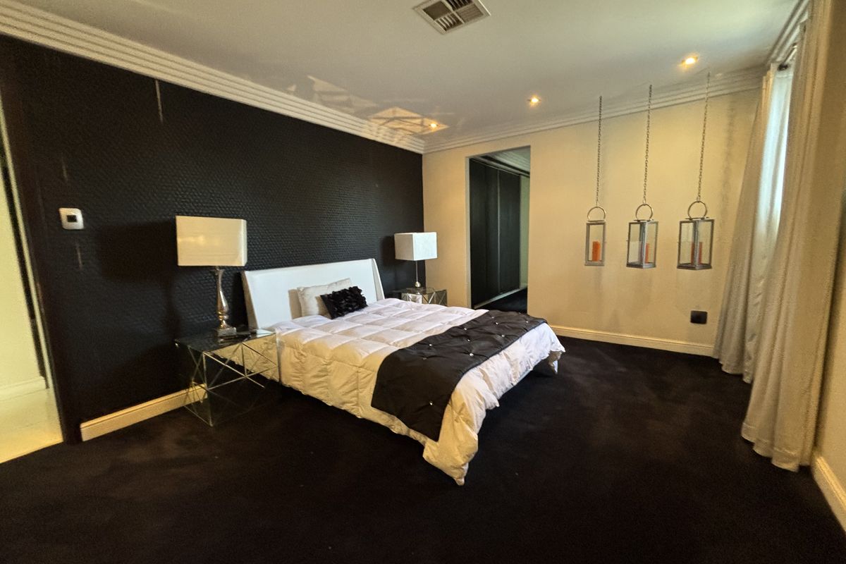 Spacious bedroom featuring dark textured accent wall, recessed downlighting, ducted air conditioning, and built-in wardrobe storage.