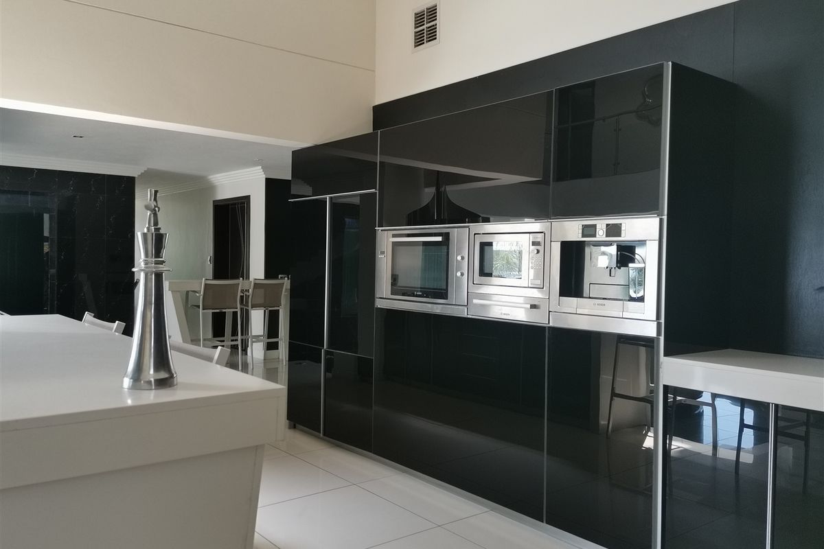 Modern kitchen featuring high-gloss black cabinetry, integrated Bosch appliances, and a sleek white kitchen island with tiled flooring.