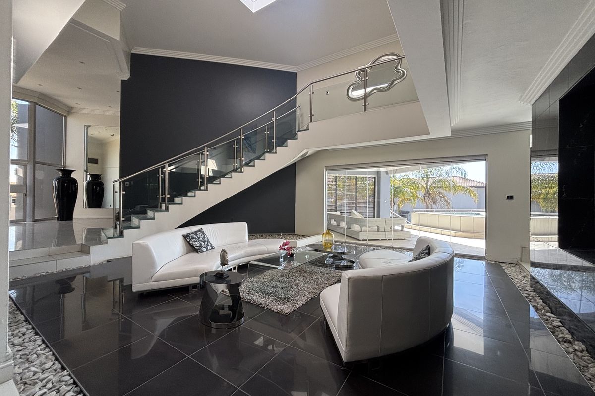 Spacious modern living room featuring a striking glass balustrade staircase, large skylight, polished dark tile flooring, and seamless access to the outdoor patio area.
