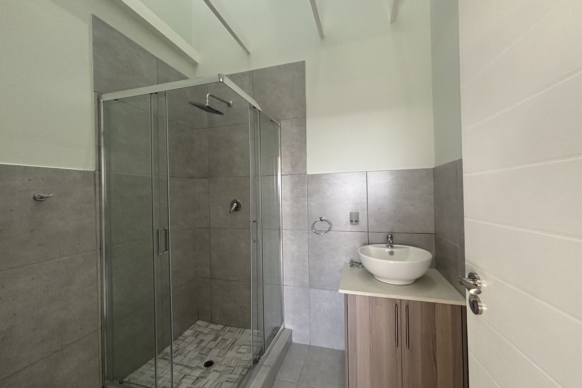 Modern bathroom featuring a glass-enclosed shower with grey wall tiles and a vanity unit with a countertop basin.