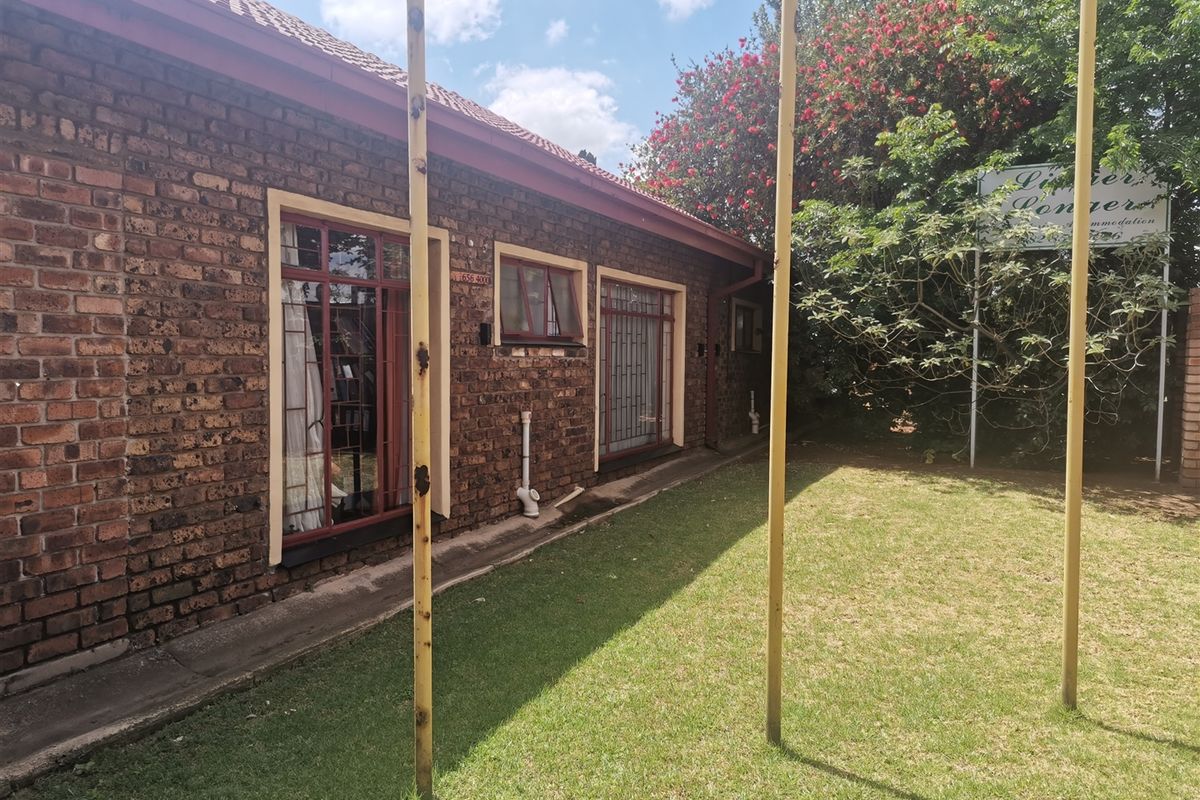Exterior view of the guest house featuring face-brick facade, tiled roof, and a surrounding lawn area with metal support structures.