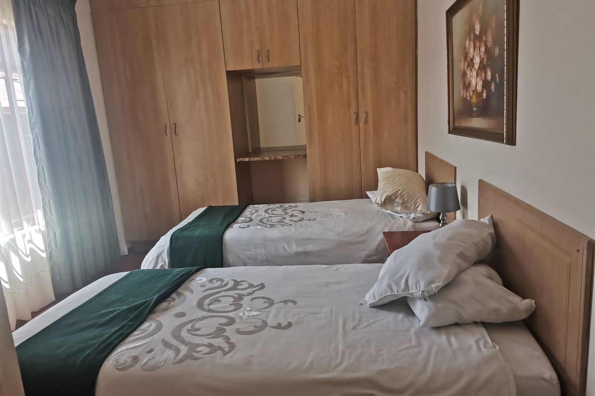 A guest bedroom featuring built-in wooden cupboards with a central vanity area and twin bed configuration.