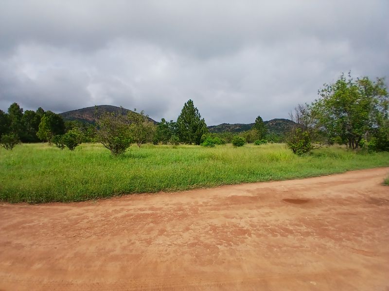 A scenic view of a rural farm landscape featuring a dirt access road, open grassy fields, and distant hills under a cloudy sky.