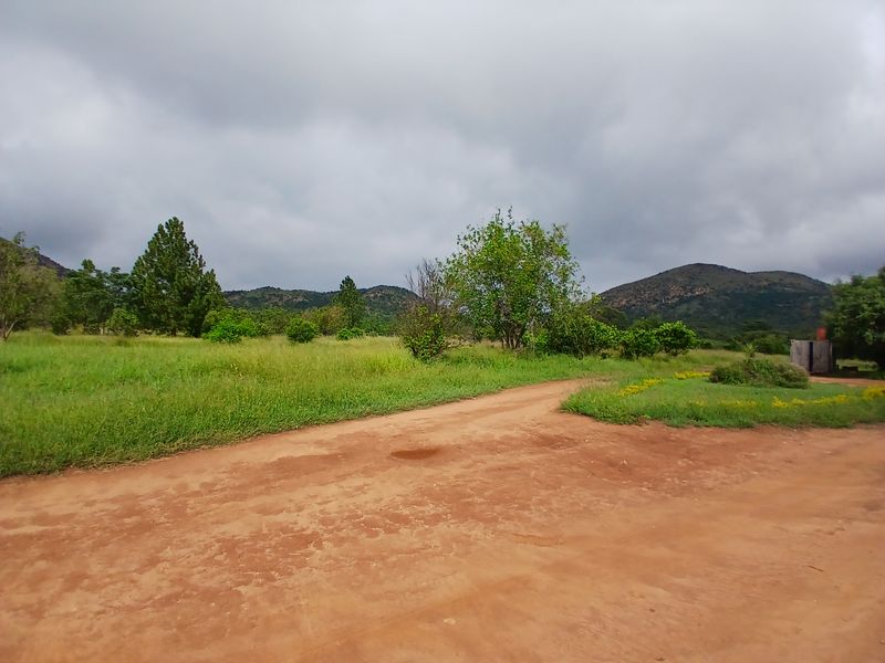 A scenic view of the farm property featuring a dirt access road, expansive open grassland, and rolling mountain hills in the background.