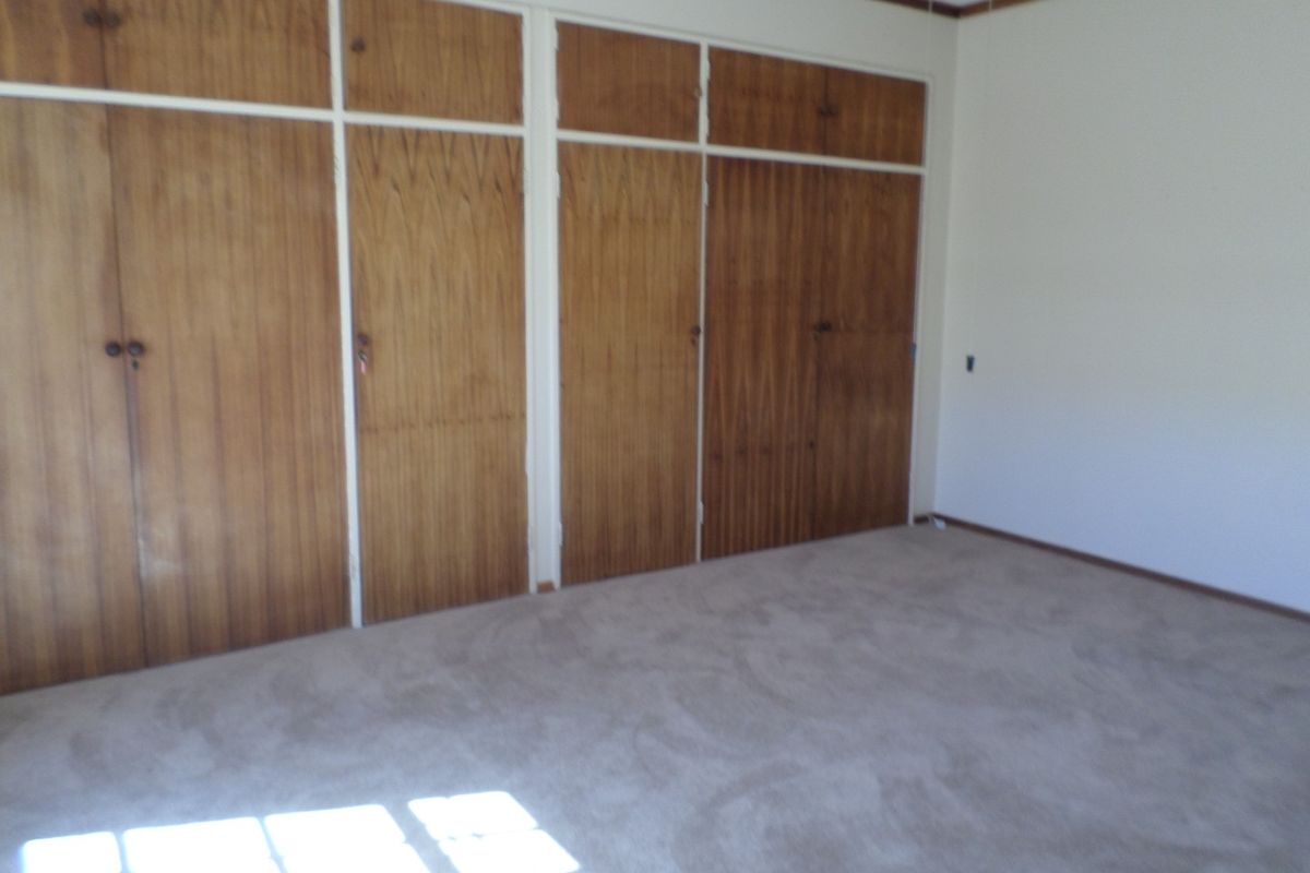 A spacious, empty bedroom featuring wall-to-wall built-in wooden cupboards and neutral carpeting, offering a blank canvas for personalization.