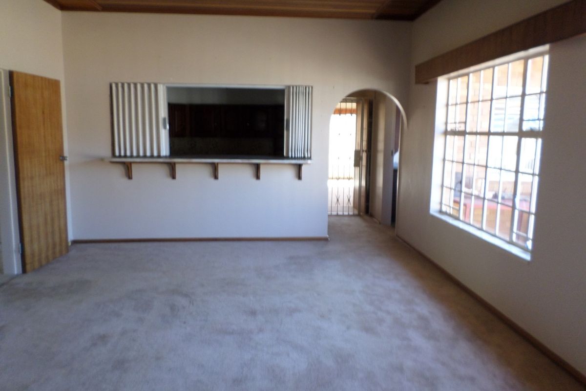 An empty living room featuring a timber ceiling, a serving hatch to the kitchen, and an arched doorway leading to an exterior security gate.