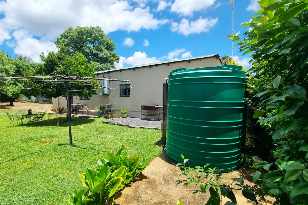 Rear garden view featuring a large green water storage tank, a rotary clothesline, and a paved patio area adjacent to the house.