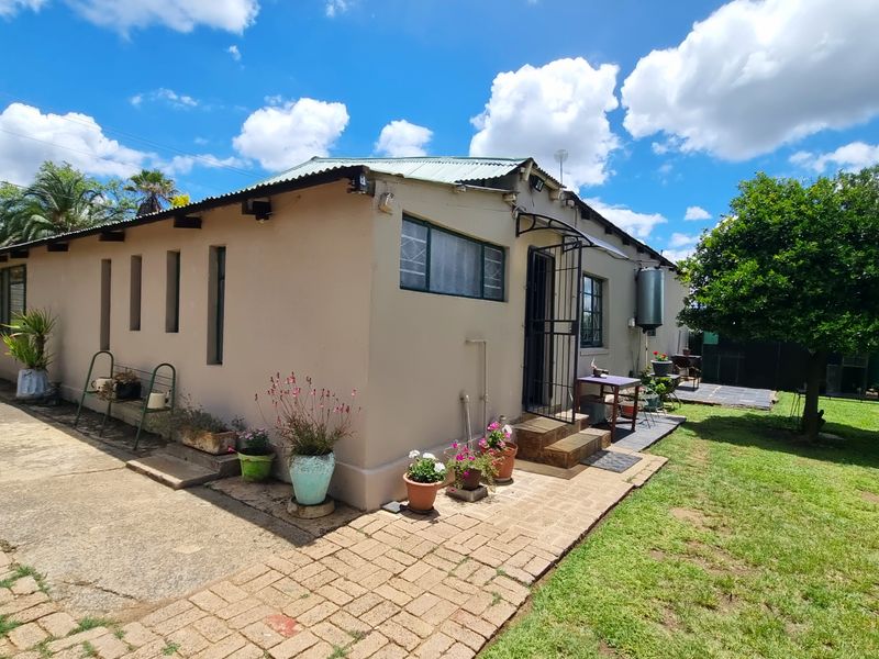 Rear view of the house featuring a paved walkway, corrugated metal roof, and external geyser, set within a garden area.