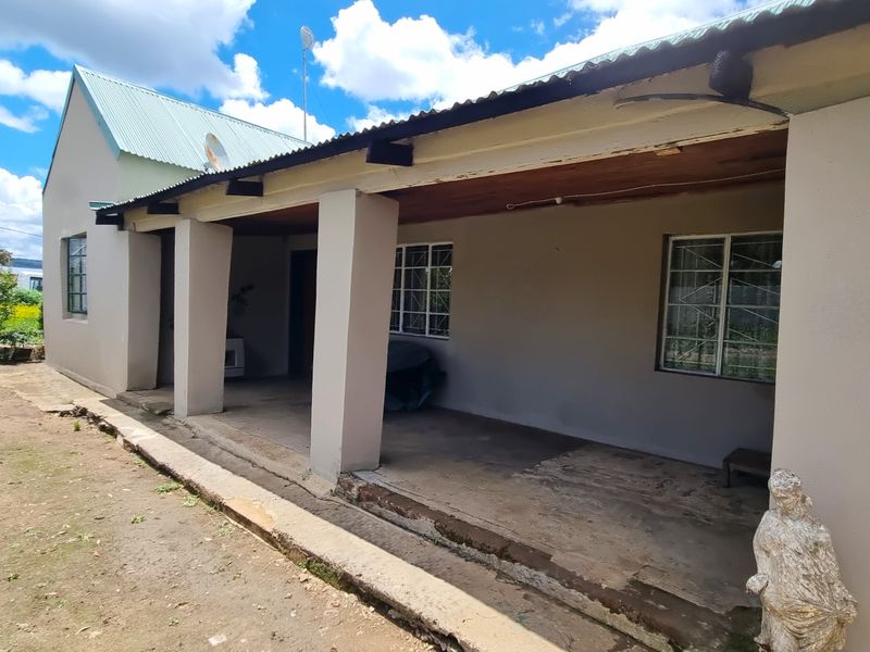 A covered outdoor patio area featuring concrete pillars and security-barred windows, requiring some maintenance to the eaves and flooring.