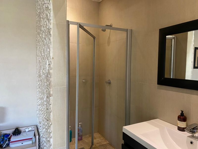 A modern bathroom featuring a glass shower enclosure, tiled walls, a mosaic feature wall, and a contemporary vanity basin.