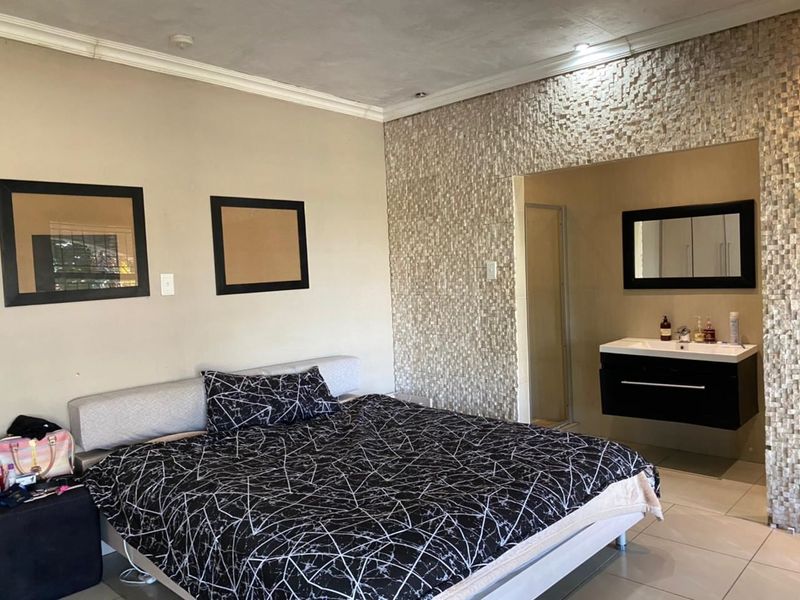 Bedroom featuring a stone-clad accent wall, integrated floating vanity, and tiled flooring, creating a modern open-plan ensuite layout.