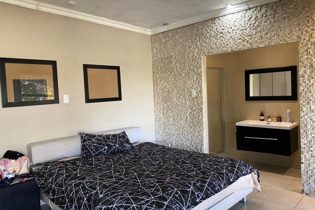 Bedroom featuring a stone-clad accent wall, integrated floating vanity, and tiled flooring, creating a modern open-plan ensuite layout.