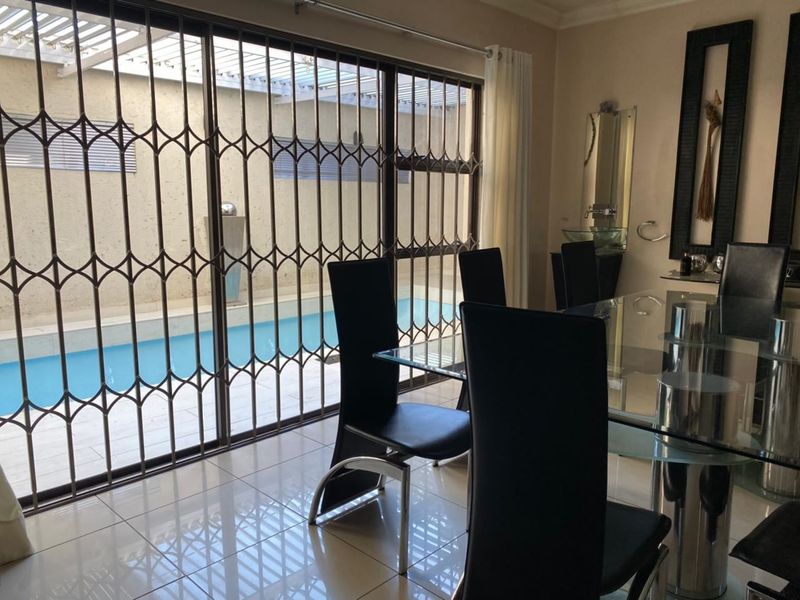 Dining area featuring tiled flooring and large sliding glass doors with security gates, providing direct access and views to the outdoor pool area.