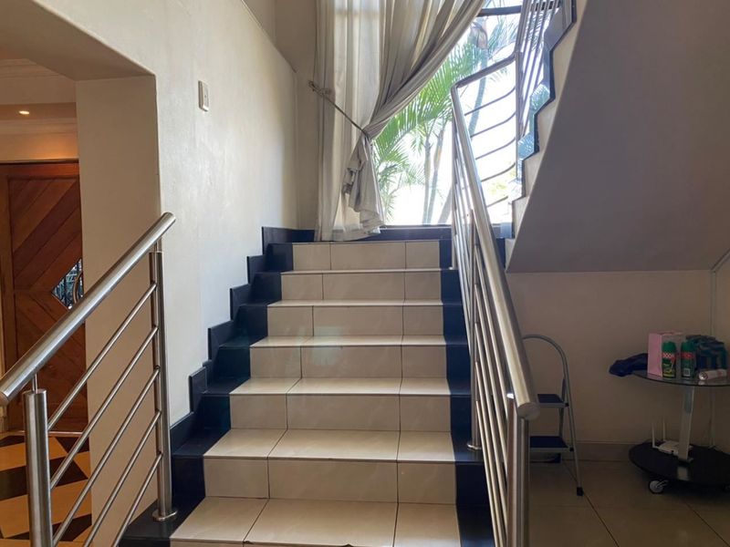 A bright hallway featuring a tiled staircase with a modern stainless steel balustrade and a large window allowing natural light.