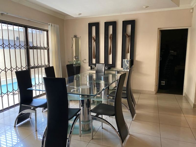 A bright dining room featuring large format floor tiles, recessed lighting, and a sliding door with security gate providing access to the pool area.