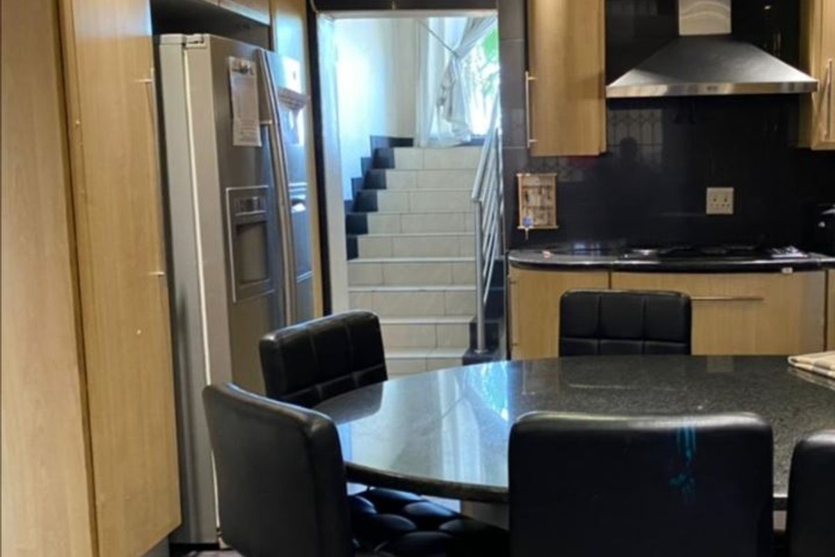 A kitchen featuring light wood cabinetry, dark stone countertops, and a stainless steel extractor fan, with an adjacent staircase leading to another level.