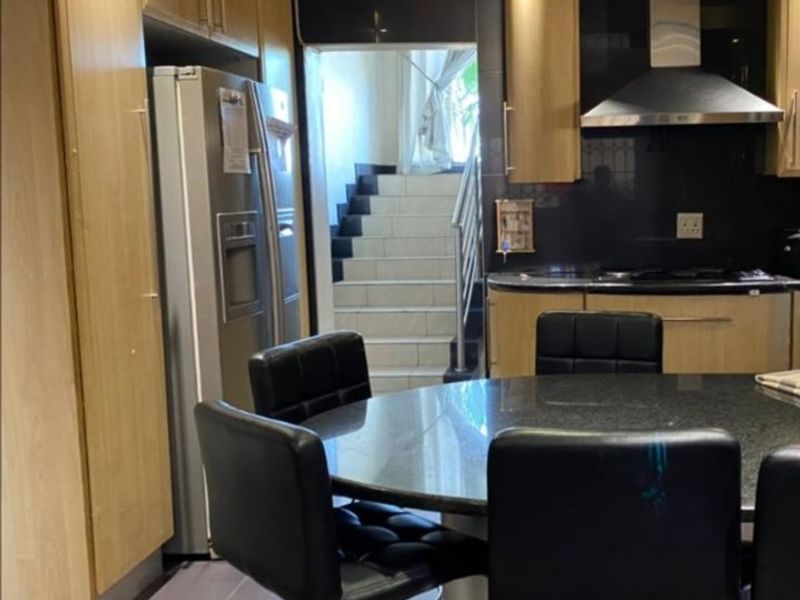 A kitchen featuring light wood cabinetry, dark stone countertops, and a stainless steel extractor fan, with an adjacent staircase leading to another level.