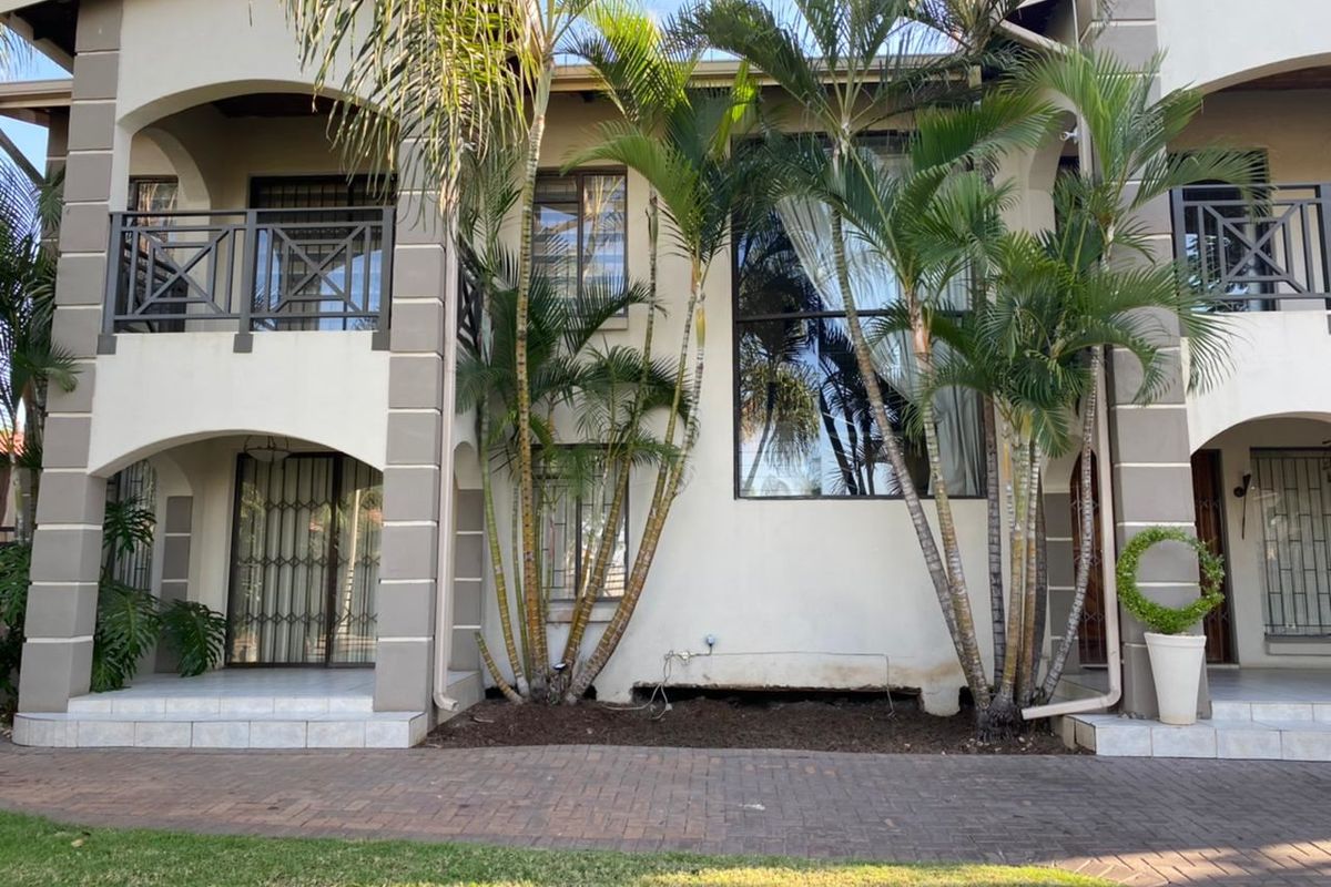 Rear elevation of a multi-story residential property featuring tiled patios, metal balustrades, and paved outdoor areas with established palm trees.