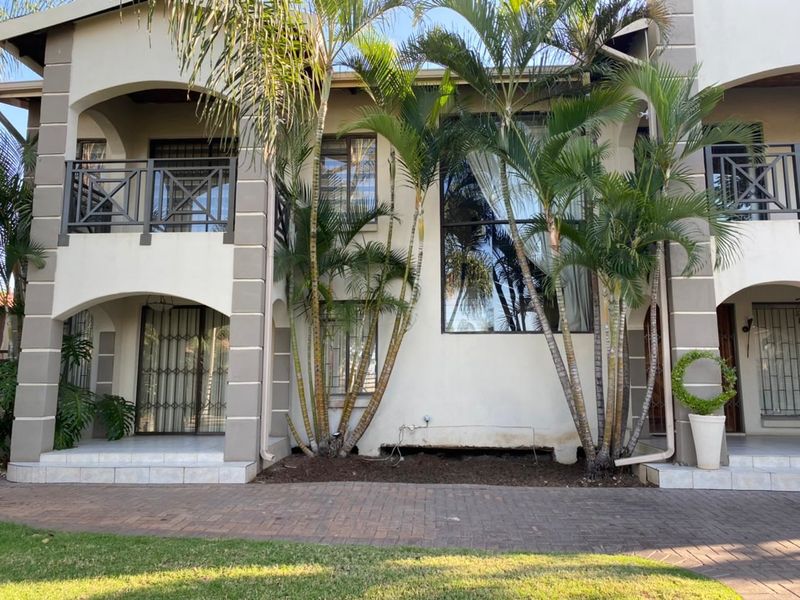 Rear elevation of a multi-story residential property featuring tiled patios, metal balustrades, and paved outdoor areas with established palm trees.
