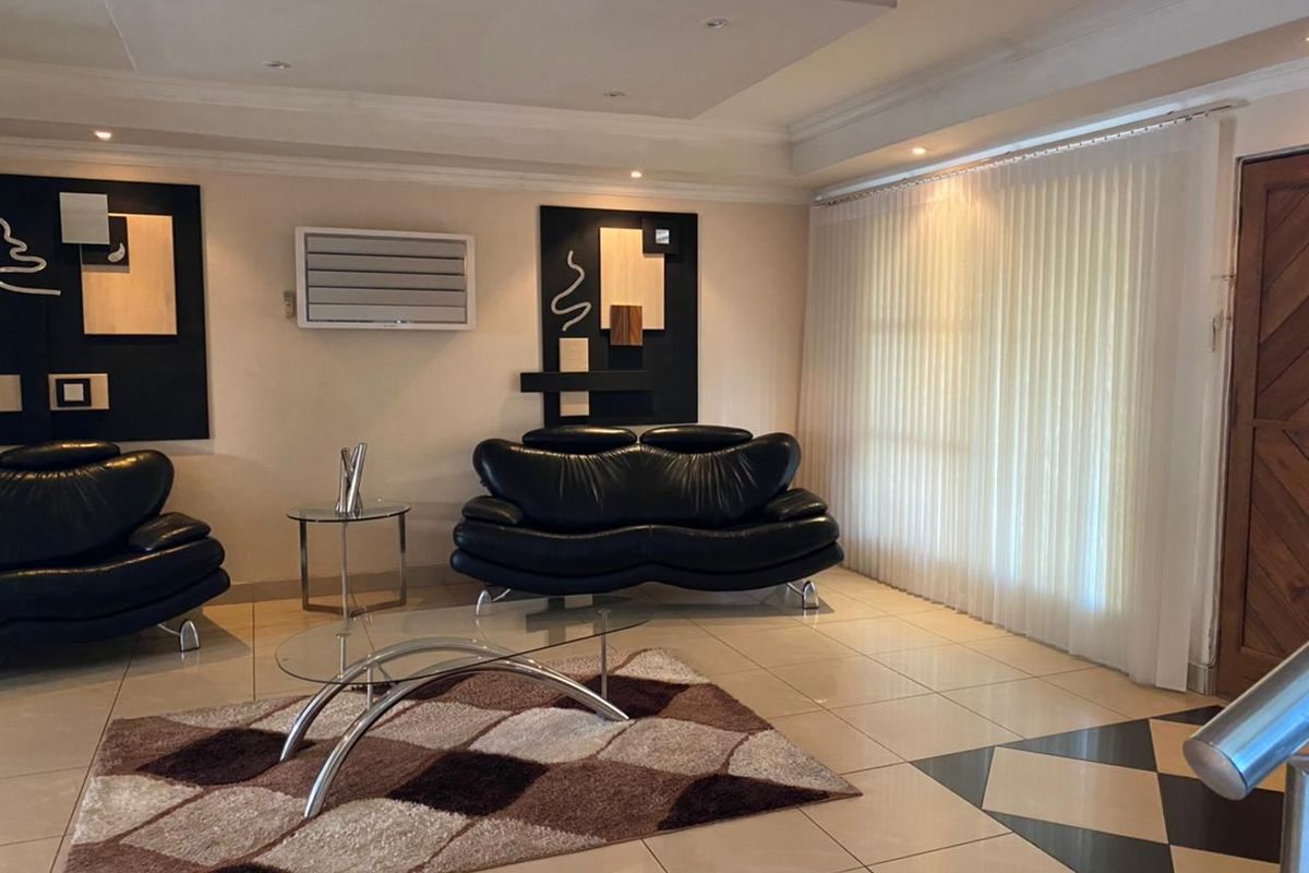 A well-maintained living room featuring tiled flooring, recessed ceiling lighting, and a wall-mounted air conditioning unit, providing a comfortable and functional living space.