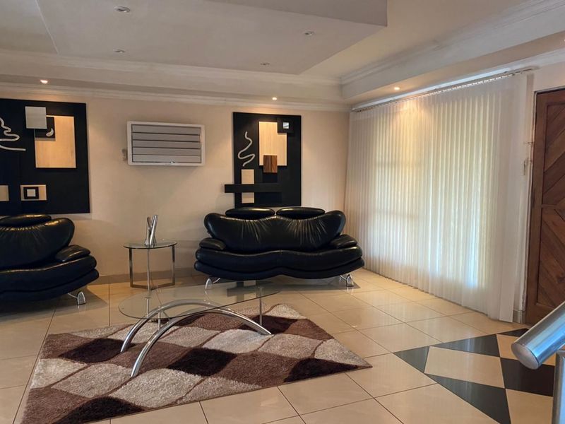 A well-maintained living room featuring tiled flooring, recessed ceiling lighting, and a wall-mounted air conditioning unit, providing a comfortable and functional living space.