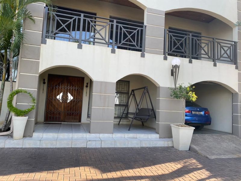Front facade of a multi-level house featuring an arched entrance, tiled porch, upper balcony with metal railings, and a covered parking area.