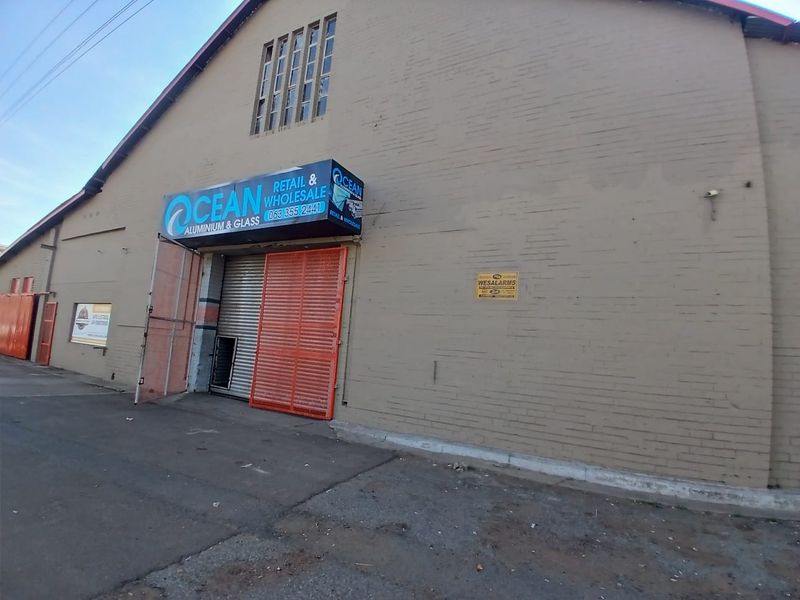 Front exterior view of a retail warehouse property featuring a roller shutter door, security gate, and prominent business signage.