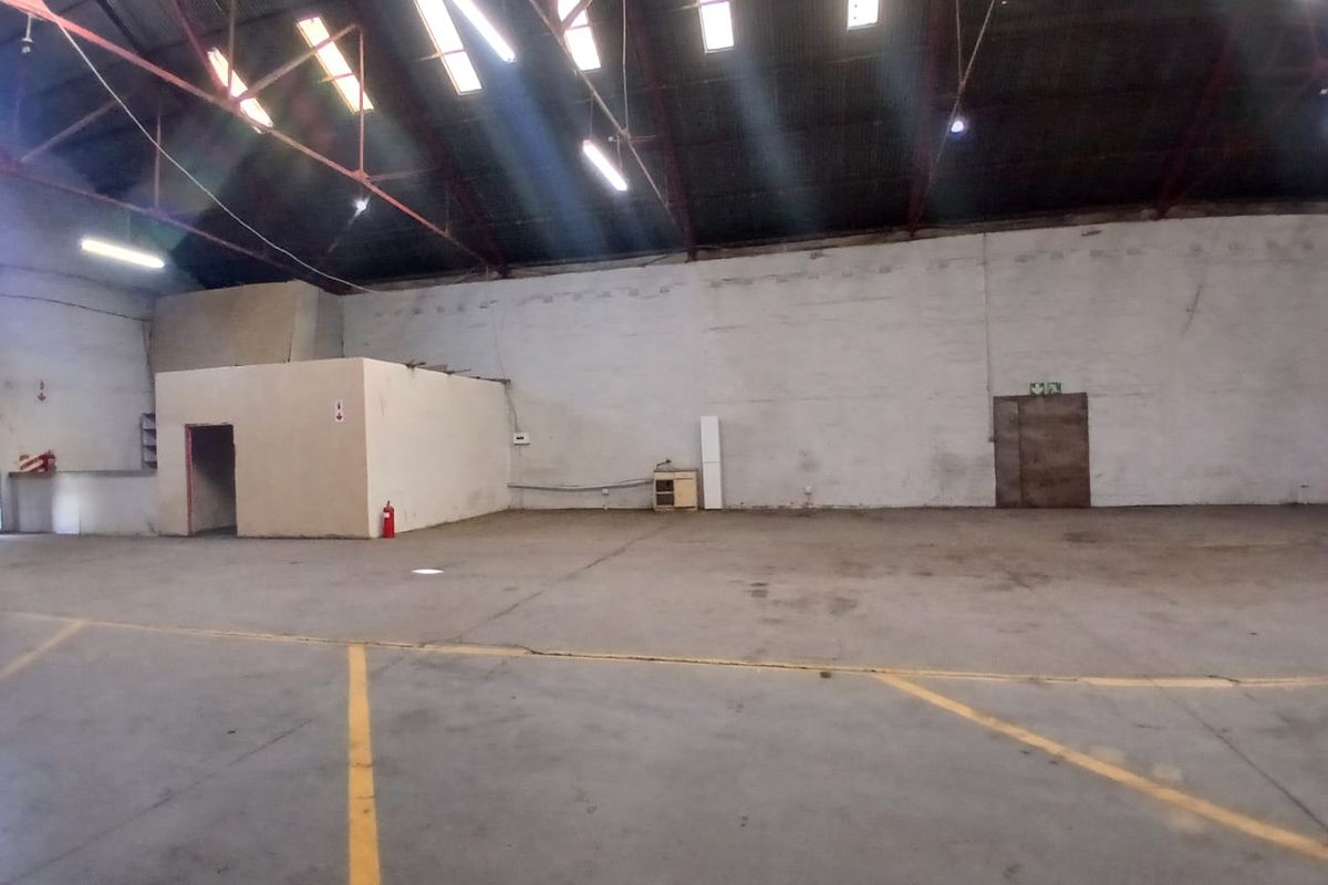 Spacious industrial utility area featuring high ceilings with exposed steel trusses, skylights, concrete flooring, and an internal partitioned office structure.