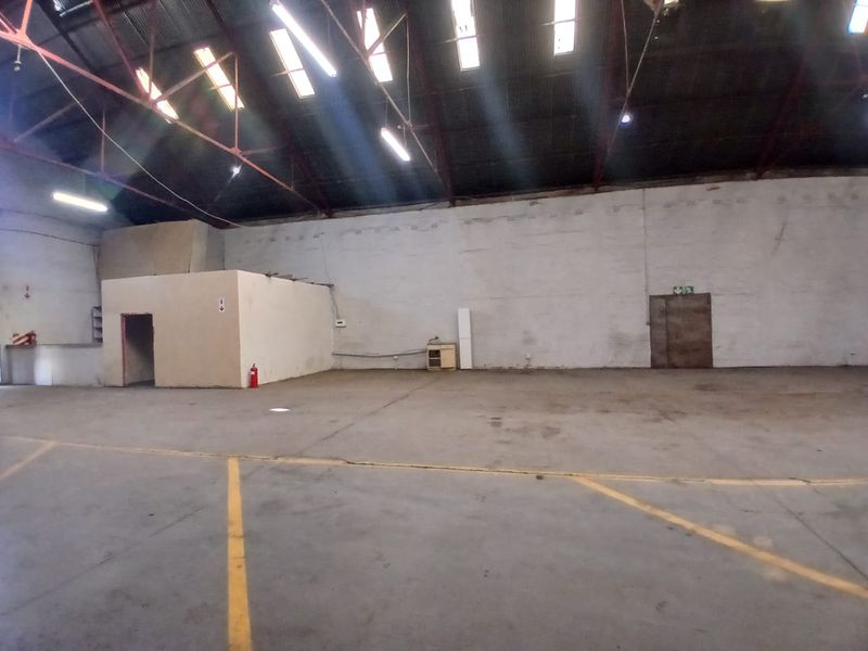 Spacious industrial utility area featuring high ceilings with exposed steel trusses, skylights, concrete flooring, and an internal partitioned office structure.