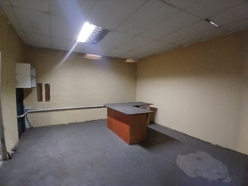 A vacant utility or retail space featuring a suspended ceiling, concrete flooring, and a built-in service counter, requiring cosmetic refurbishment.